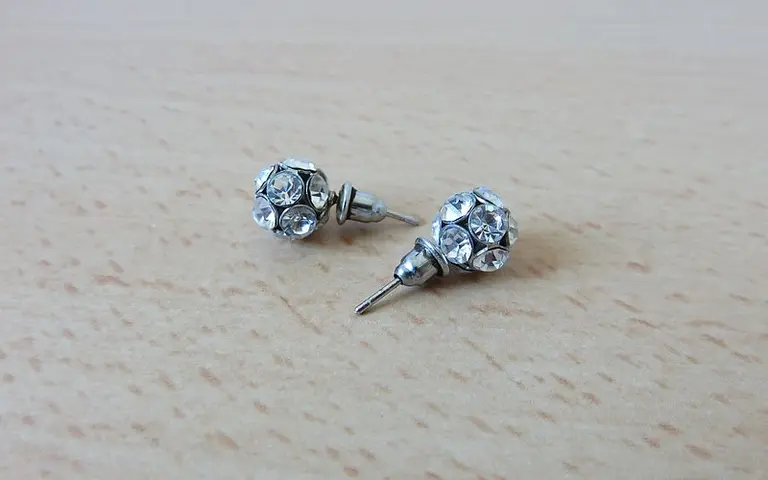 Zwei silberne Ohrstecker mit funkelnden, klaren Schmucksteinen, die in einer runden Form angeordnet sind. Sie liegen auf einer Holzoberfläche und sind leicht versetzt dargestellt.