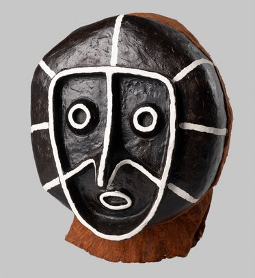 Eine stilisierte Maske aus Keramik mit einer schwarzen Oberfläche und weißen, geometrischen Linien. Die Maske hat große runde Augen und einen offenen Mund, der emotionale Ausdruck zeigt. Sie ist auf einer braunen Basis platziert und vermittelt einen Eindruck von kultureller Kunst.
