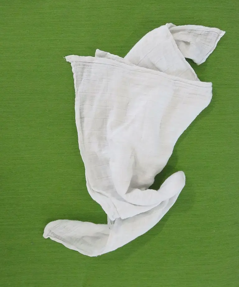 Ein zerknittertes, weißes Tuch liegt auf einem grünen Hintergrund. Das Tuch ist unregelmäßig gefaltet und zeigt eine leichte Textur.