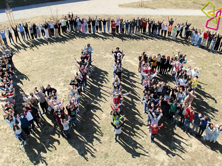 Eine große Gruppe von Menschen steht im Freien und formt mit ihren Körpern die Buchstaben