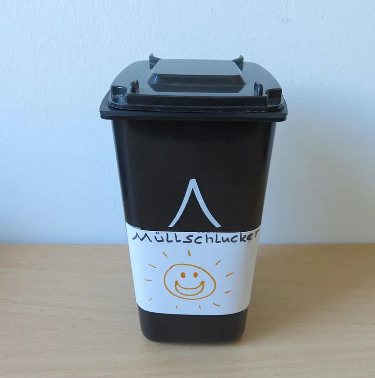 Ein schwarzer Müllbehälter mit einem weißen Aufkleber, auf dem das Wort