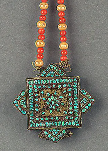 Eine Halskette mit einem quadratischen Anhänger, der mit blaugrünen Steinen verziert ist. Der Anhänger hat eine geometrische Musterung und hängt an einer Kette aus farbigen Perlen in Rot und Gold.