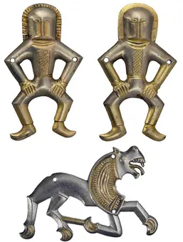 Three decorative metal pieces are shown: two human figures positioned with hands on hips, one in gold and one in silver, and a silver figure of a lion with a fierce expression. The designs are stylized and feature intricate details.