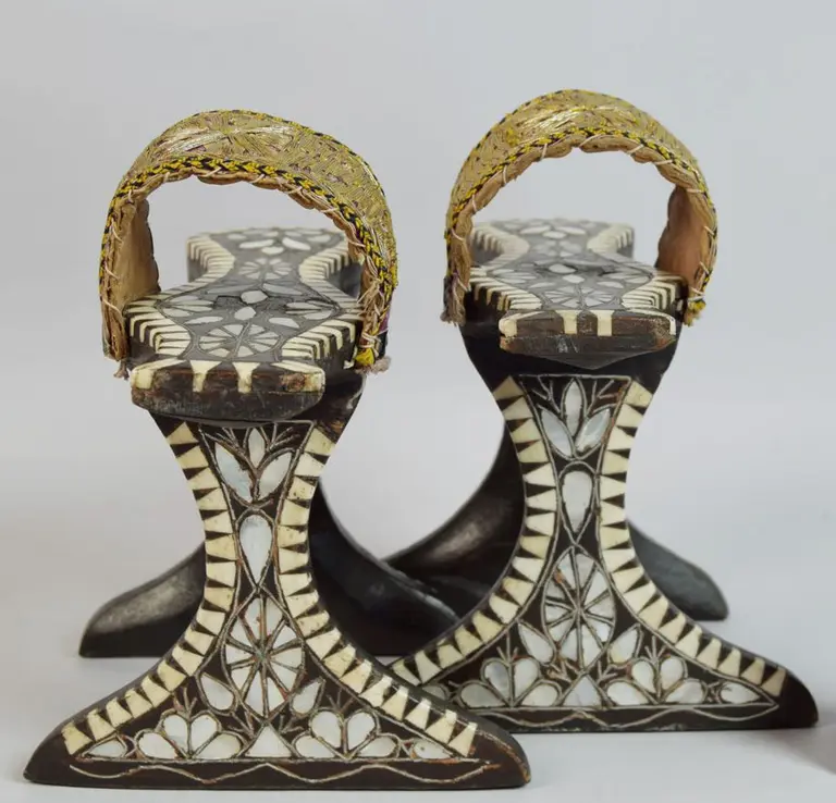 Zwei kunstvoll verzierte Holzsandalen stehen nebeneinander. Die Sohle ist mit geometrischen Mustern verziert und hat eine auffällige, geflochtene Oberseite. Diese traditionellen Sandalen zeigen ein einzigartiges, handgearbeitetes Design.