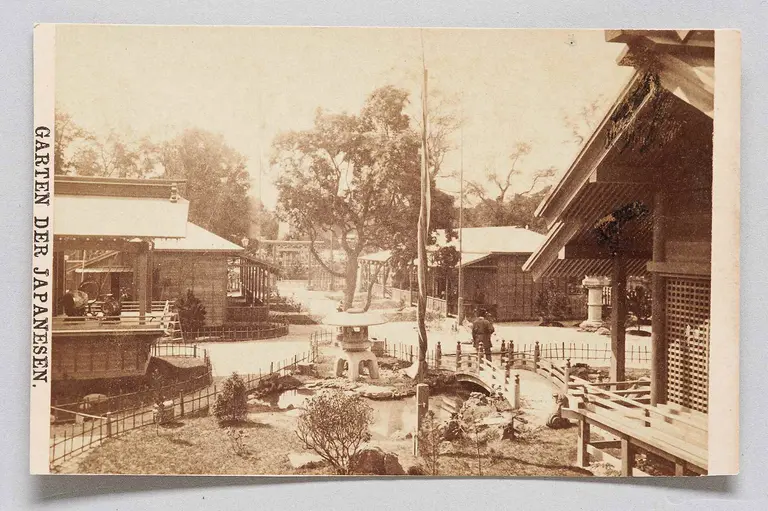 The image depicts a traditional Japanese garden, featuring wooden structures, a stone lantern, and landscaped paths. Trees and shrubs are strategically placed, contributing to the serene atmosphere of the garden. The setting reflects an aesthetic design typical of Japanese architecture and nature integration.