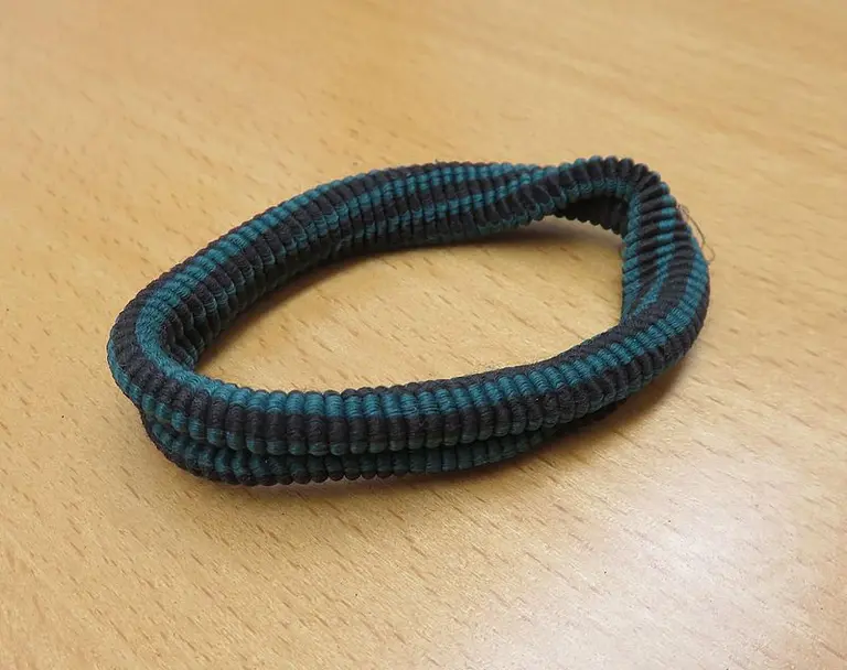 Ein elastisches Haarband in Blau- und Grüntönen liegt auf einer Holzoberfläche. Es hat eine mehrfache Wicklung und ist flexibel.