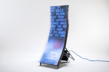 Ein auf einem Ständer stehendes, durchsichtige Display mit leicht geschwungener Oberfläche, auf dem verschwommene Textzeilen in blauer Schrift angezeigt werden. Der Bildschirm wirkt futuristisch und ist mit einem Kabel verbunden.