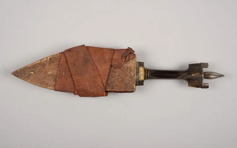 Ein historisches Messer mit einer spitzen Klinge und einem Griff, der mit braunem Leder umwickelt ist. Die Klinge ist aus Metall und die Verbindung zum Griff ist sichtbar.
