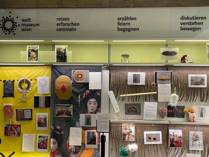 Display at the Weltmuseum Wien featuring various cultural artifacts and images. A yellow backdrop supports a collage of photographs, masks, and text, emphasizing themes of exploration, celebration, and understanding across cultures. Header text translates as