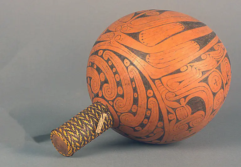 Ein traditionelles Musikinstrument in Form einer schalenartigen Hohlkugel mit reichhaltigen, geometrischen Mustern in verschiedenen Brauntönen. Der Griff ist mit geflochtenem Material umwickelt und zeigt eine Verbindung zwischen Kunst und Handwerkskunst.