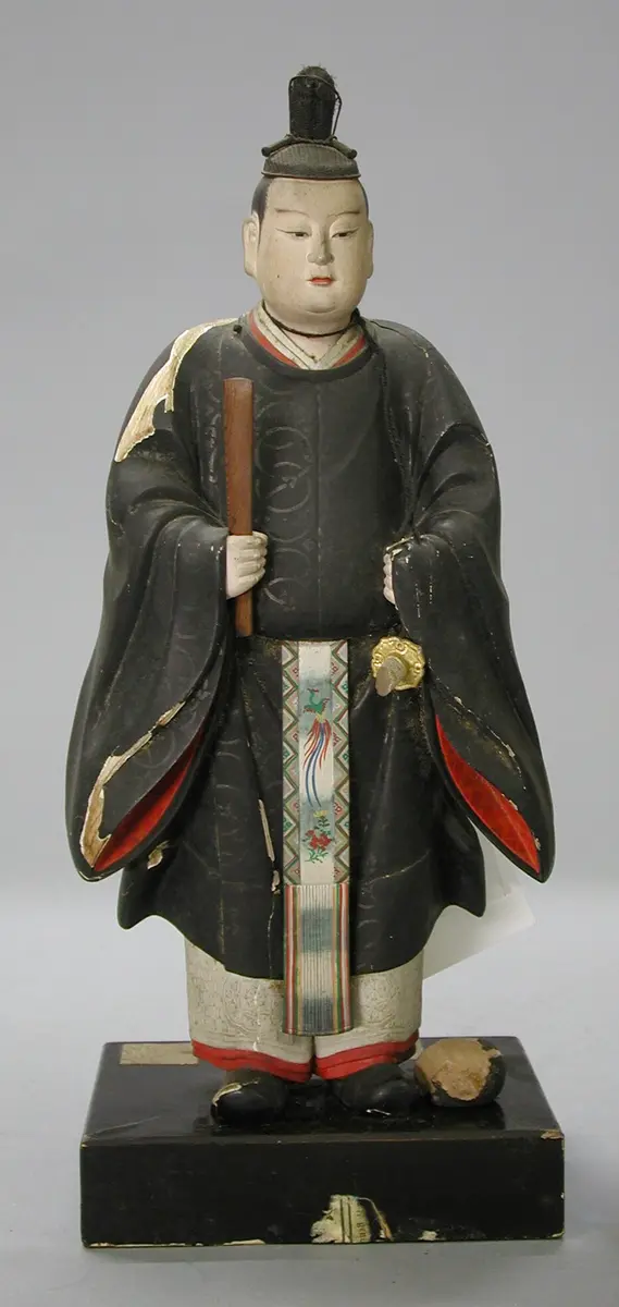 A traditional Japanese figure stands upright, wearing a black robe with red accents and intricate details. The figure holds a stick in one hand and features a stylized hairstyle. It is placed on a black base, emphasizing its historical significance and craftsmanship.