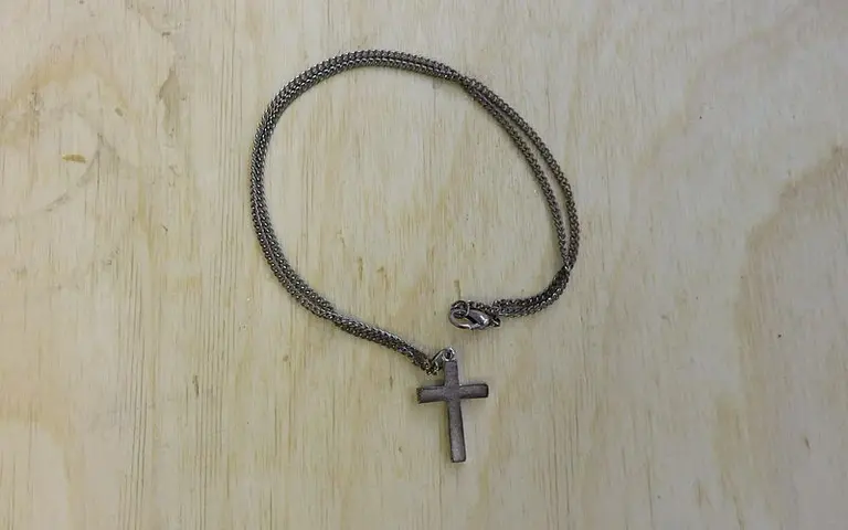 Das Bild zeigt ein silbernes Armband mit einer kleinen Kreuzanhänger. Das Armband hat eine enge, glatte Kette und ist auf einem hellen Holzuntergrund platziert.