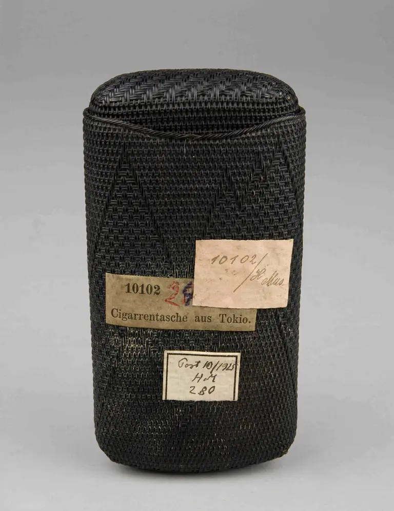 A cylindrical black pouch made of woven material, featuring a lid at the top. Attached labels include numbers and the phrase 
