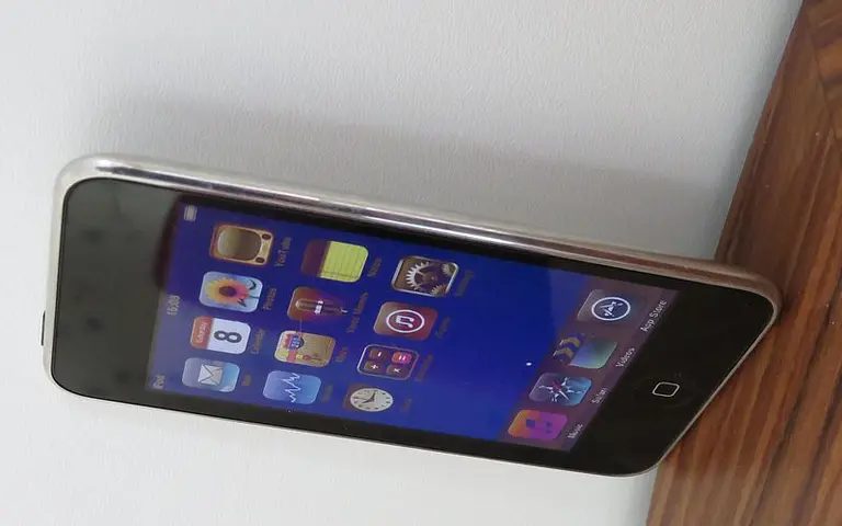 Ein seitlich stehendes Smartphone zeigt einen bunten Bildschirm mit verschiedenen App-Icons. Die Icons sind klar erkennbar und umfassen Anwendungen für Kommunikation, Medien und Wetter. Der Hintergrund des Bildschirms ist dunkelblau.