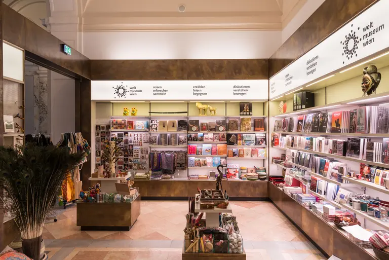 Das Bild zeigt den Verkaufsraum eines Museums mit Regalen, die eine Vielzahl von Büchern und Souvenirs ausstellen. Im Raum sind eine große Auswahl an kulturellen Artikeln und Geschenkideen sichtbar, ergänzt durch dekorative Elemente wie Pflanzen.