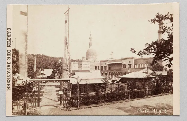 The image features a historical view of a Japanese garden, showcasing traditional structures surrounded by lush greenery. In the background, a pagoda-like building stands tall, signifying an authentic cultural atmosphere. The scene conveys a serene outdoor space typical of Japanese aesthetics.