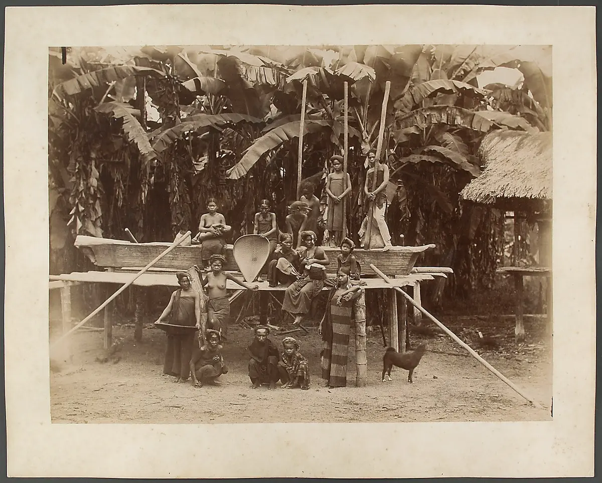 Women and children of the Batak Karo in front of a contraption upon which the women stamp rice