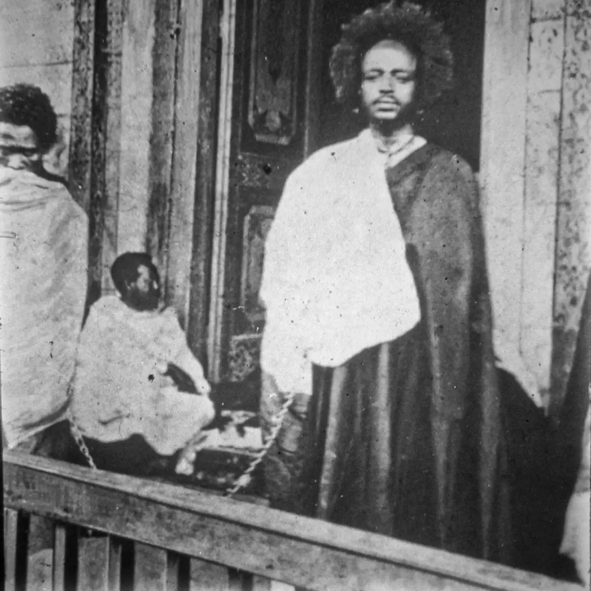 Tato Gaki Sheroko als Gefangener von Menelik II. in Addis Abeba, mit silberner Kette an seinen Bewacher Aarau gefesselt. Links im Hintergrund: der späte äthiopische Gouverneur Wolde Giyorgis.