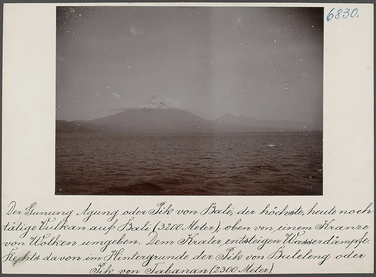 Der Gunung Agung oder Pik von Bali, der höchste, heute noch tätige Vulkan auf Bali (3200 m); oben von einem Kranze von Wolken umgeben. Dem Krater entsteigen Wasserdämpfe. Rechts davon im Hintergrunde der Pik von Buleleng oder Pik von Tabanan (2300 m)