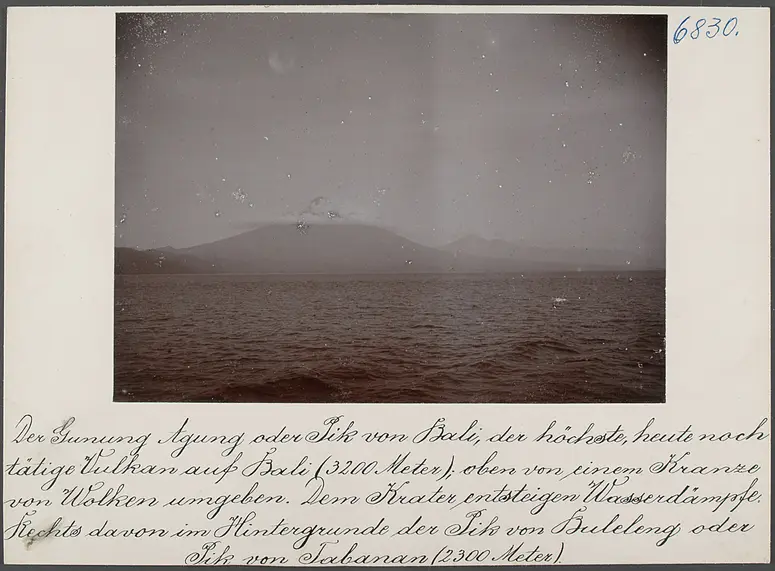 Der Gunung Agung oder Pik von Bali, der höchste, heute noch tätige Vulkan auf Bali (3200 m); oben von einem Kranze von Wolken umgeben. Dem Krater entsteigen Wasserdämpfe. Rechts davon im Hintergrunde der Pik von Buleleng oder Pik von Tabanan (2300 m)